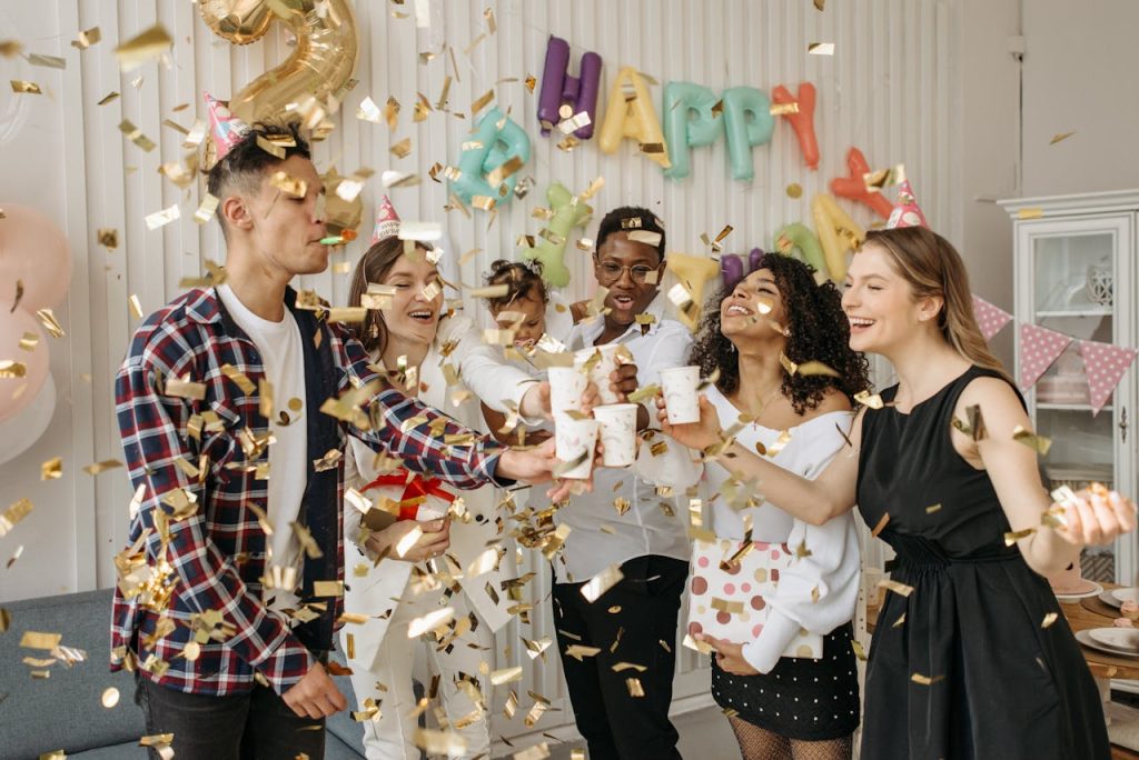 family-and-group-of-friends-celebrating-a-child-s-birthday-7180617 A lively indoor birthday party with friends celebrating with confetti and drinks in a decorated room.
