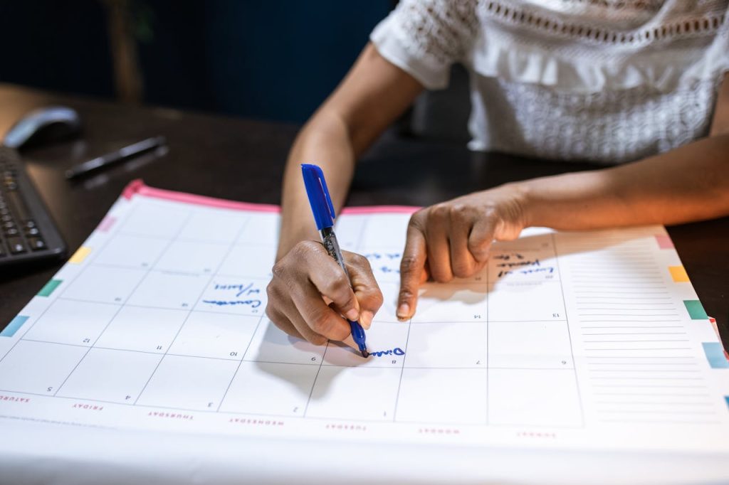 person-writing-on-paper-calendar-6170652 A woman marks important dates on her desk calendar, planning upcoming events.